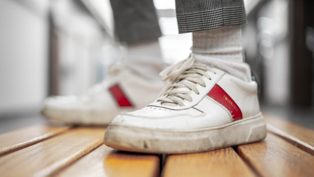 a person standing on a wooden floor wearing white and red sneakers